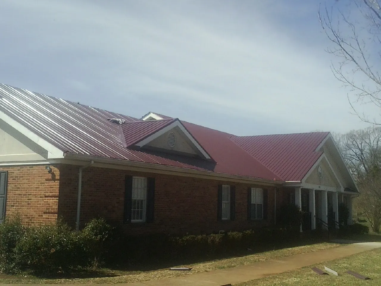 Red metal roof with gabled entries on a long brick building, from a Hail Damage Roof Repair job in Wilton