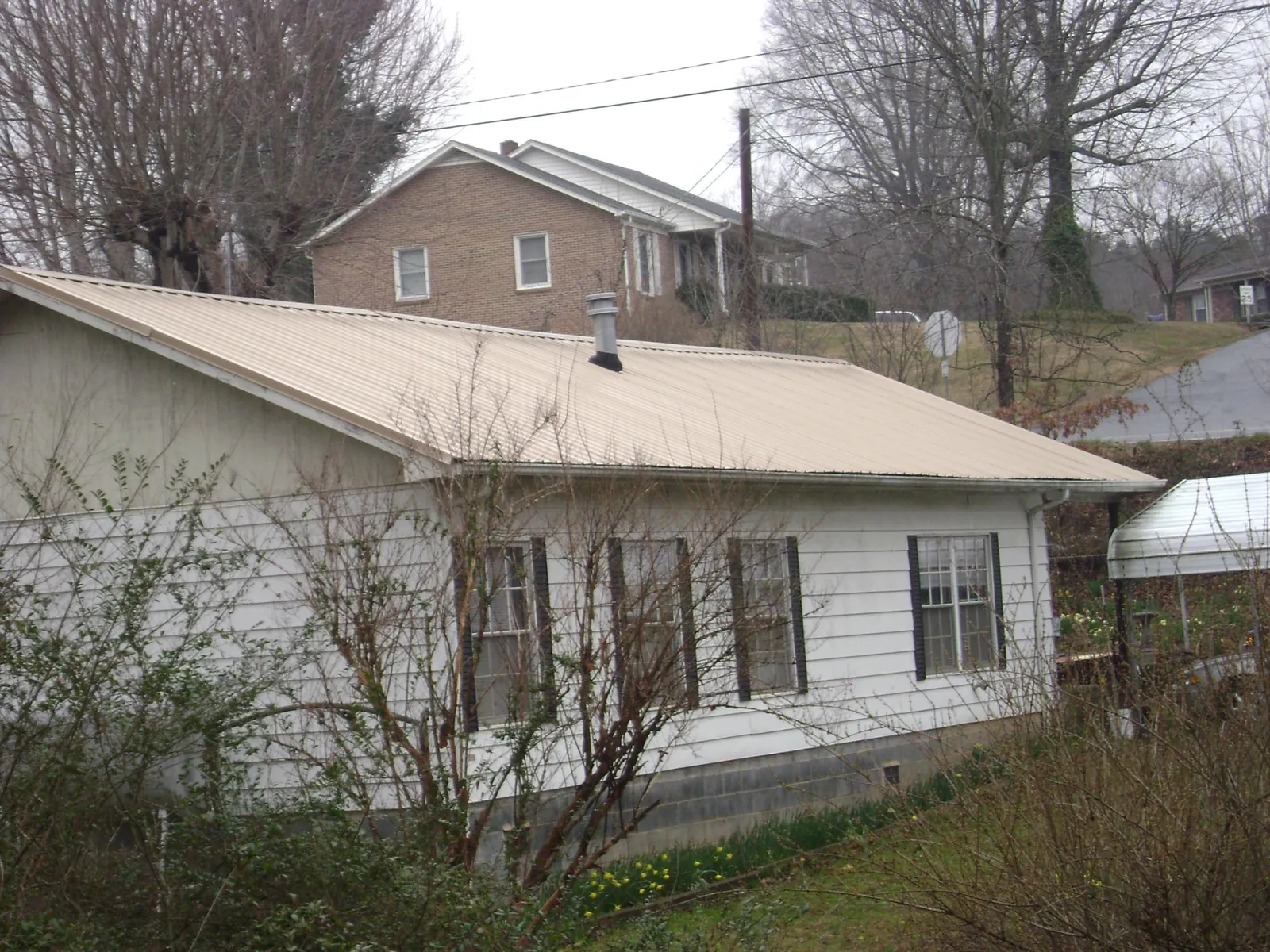 Tan metal roof on a white sided house set into a hillside — Commercial Roofing by Roofing Brothers in Wilton